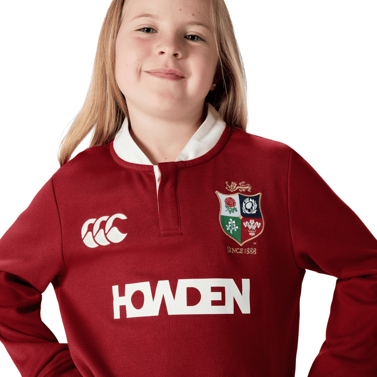 A young person confidently poses against a white background, wearing the Youth British &amp; Irish Lions 2025 Long Sleeve Classic Jersey by Canterbury. This jersey features logos and moisture-wicking fabric for comfort and style.