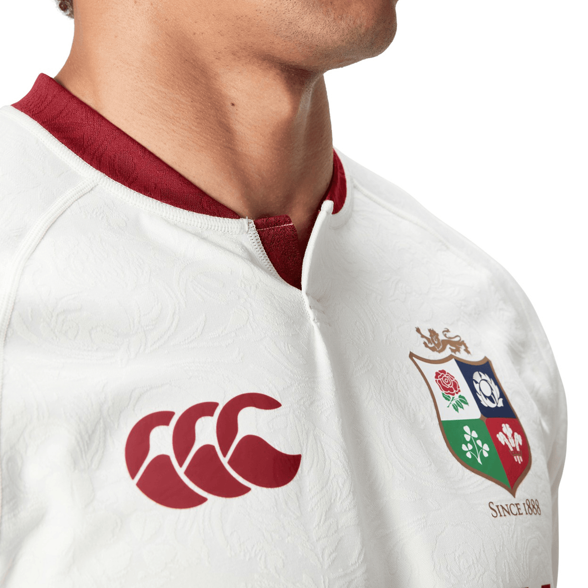 Close-up of a person wearing the British &amp; Irish Lions 2025 Training Jersey by Canterbury in white with red details, highlighting ergonomically positioned panels for added comfort. The jersey prominently displays the Canterbury logo along with the British &amp; Irish Lions emblem, reflecting the design of the official replica training jersey.