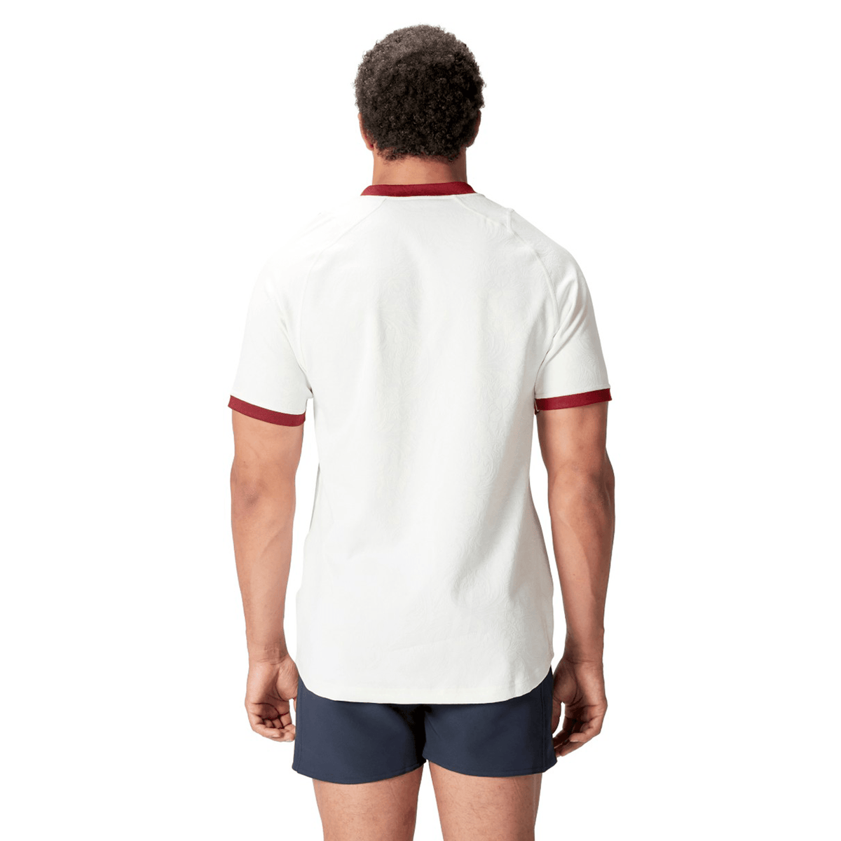 A person wearing the British &amp; Irish Lions 2025 Training Jersey by Canterbury, featuring a white design with red trim, along with dark shorts, stands with their back to the camera.