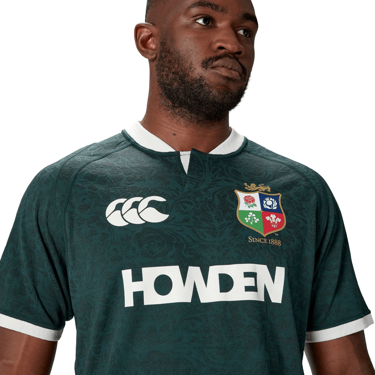 A man wearing the British &amp; Irish Lions 2025 Training Jersey by Canterbury, featuring logos and "Howden" text. This stylish, dark green piece is crafted from recycled polyester for an eco-friendly touch.