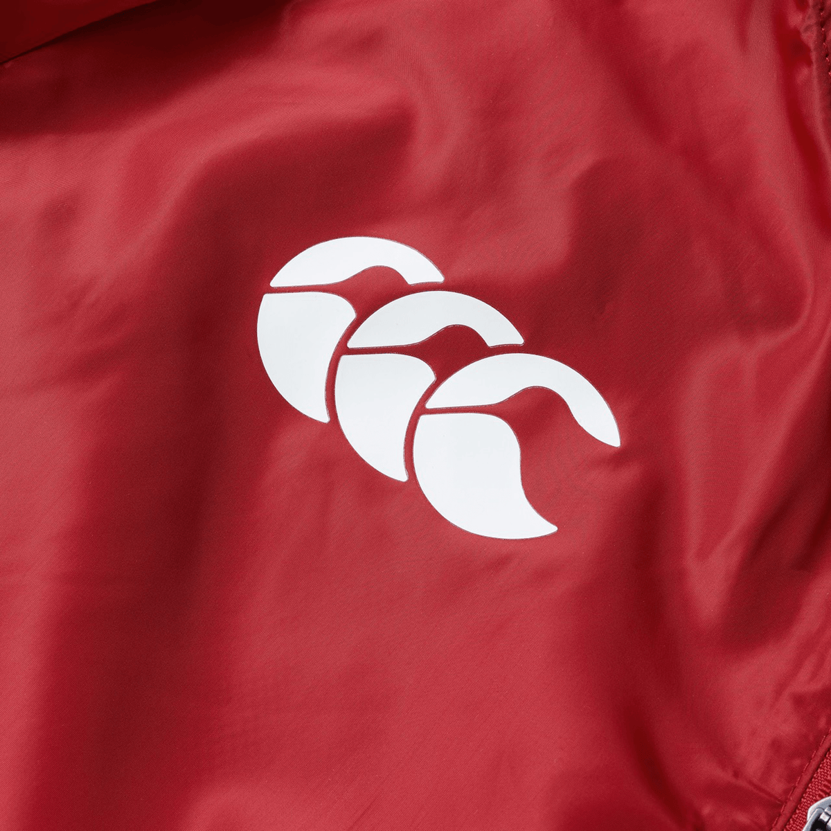 Close-up of a red fabric from the British &amp; Irish Lions 2025 Lightweight Rain Jacket by Canterbury, featuring the white logo with three overlapping crescent shapes.