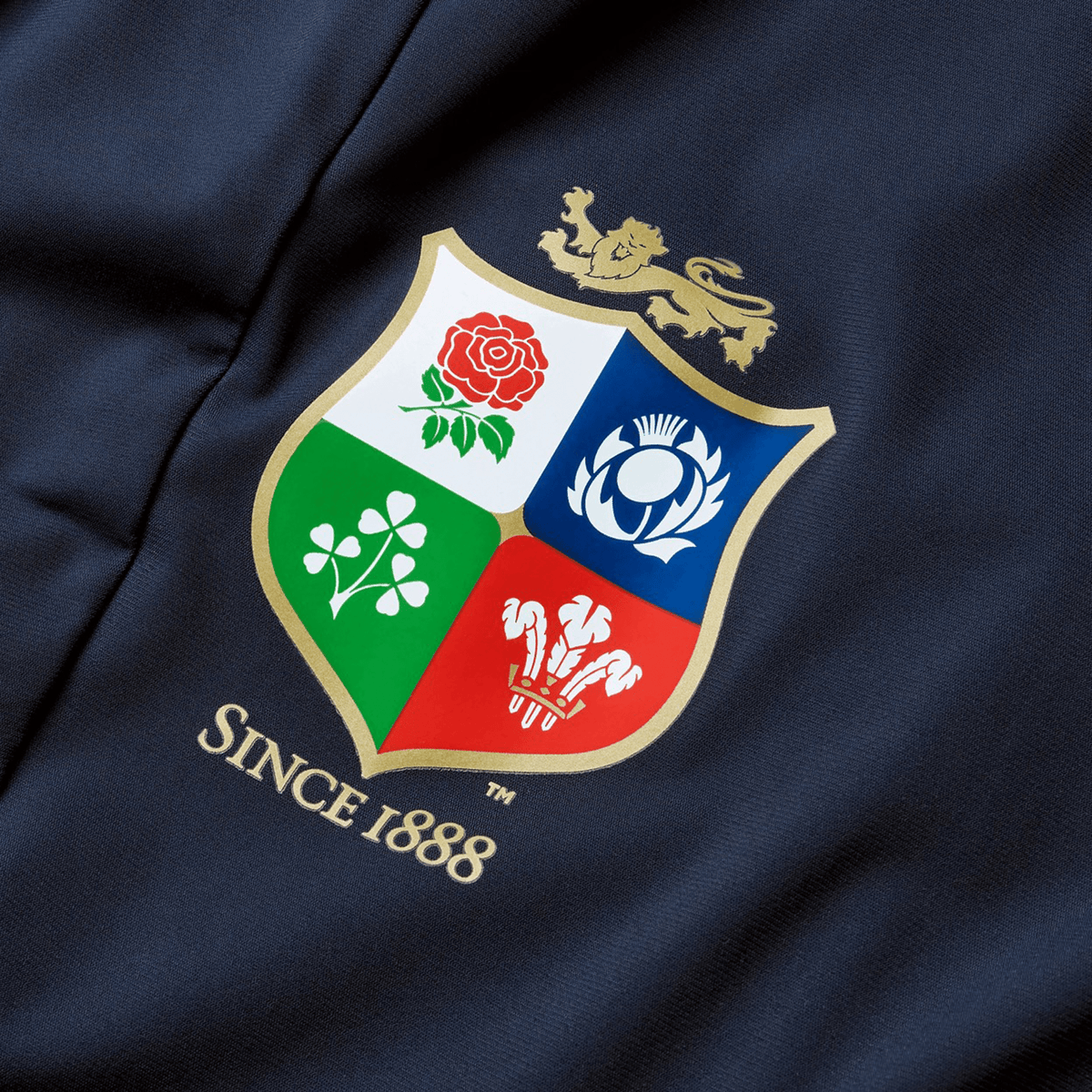 The British &amp; Irish Lions 2025 Everest Woven Pant by Canterbury is designed with a navy fabric displaying a coat of arms that includes a lion, rose, thistle, shamrock, and three feathers. The text "Since 1888" highlights the heritage of the British &amp; Irish Lions. Made from quick-drying fabric, it offers both durability and comfort.
