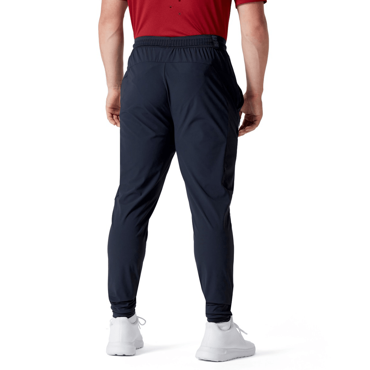 Individual in a red shirt, Canterbury's British &amp; Irish Lions 2025 Everest Woven Pant, which is crafted from four-way stretch quick-drying fabric, and white sneakers, depicted from the back on a white background.