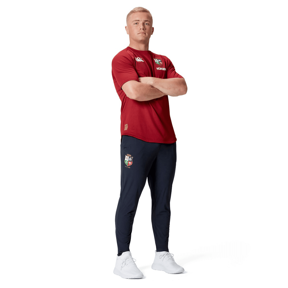 A person in a red shirt and Canterbury British &amp; Irish Lions 2025 Everest Woven Pant stands with arms crossed, looking forward.