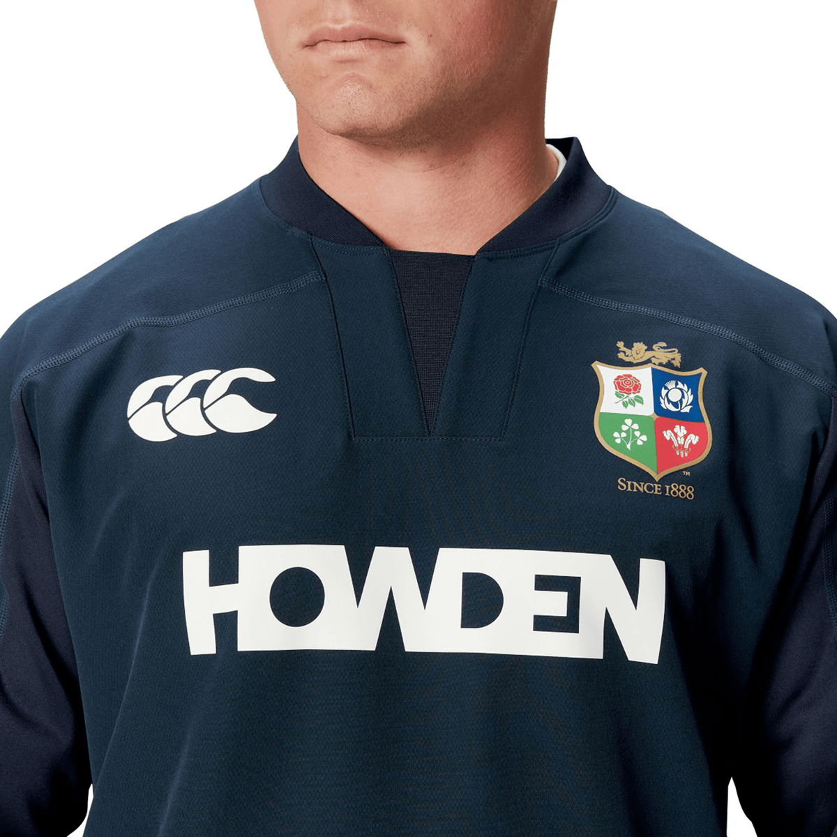 An individual wearing a dark Canterbury rugby shirt adorned with the logos and text "HOWDEN" and "SINCE 1888" on the front, showcasing the performance fit of the British &amp; Irish Lions 25 Drill Top.