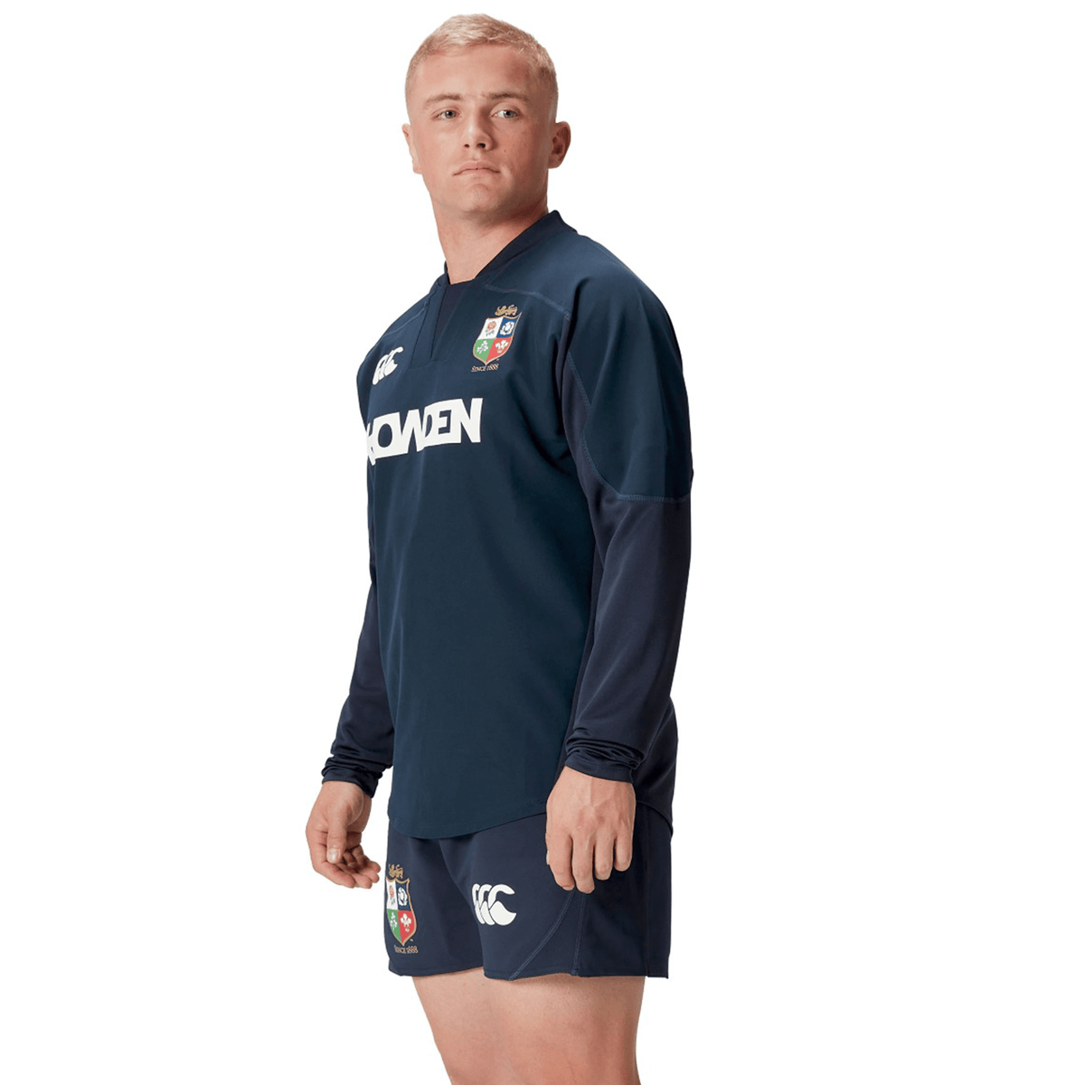 A man is wearing a navy blue British &amp; Irish Lions 25 Drill Top by Canterbury, featuring the logo and brand name on the front, designed with a performance fit for optimal comfort.