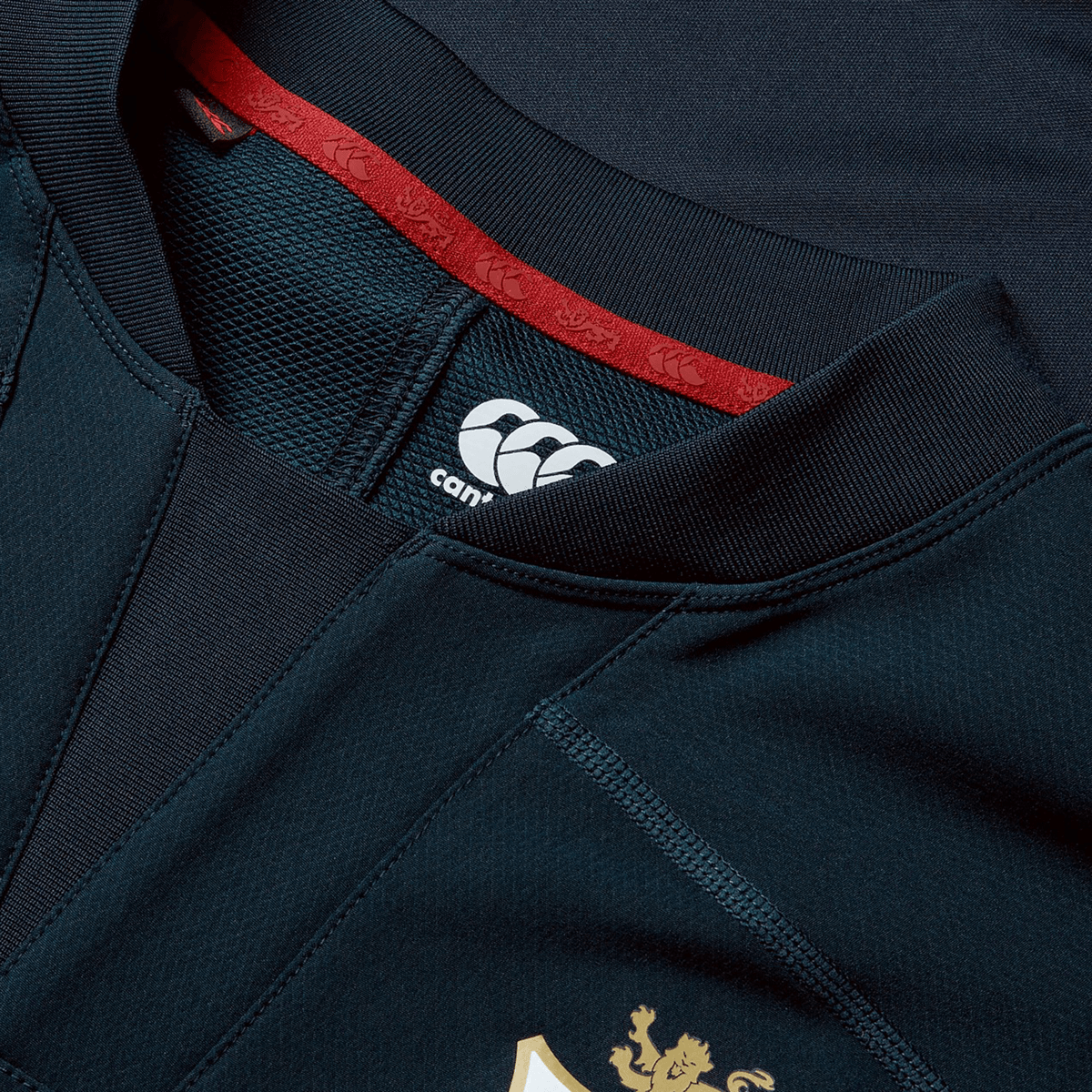 Close-up of the British &amp; Irish Lions 25 Drill Top by Canterbury, featuring a dark blue design with red accents on the inner collar and a white logo on the chest, providing a performance fit.