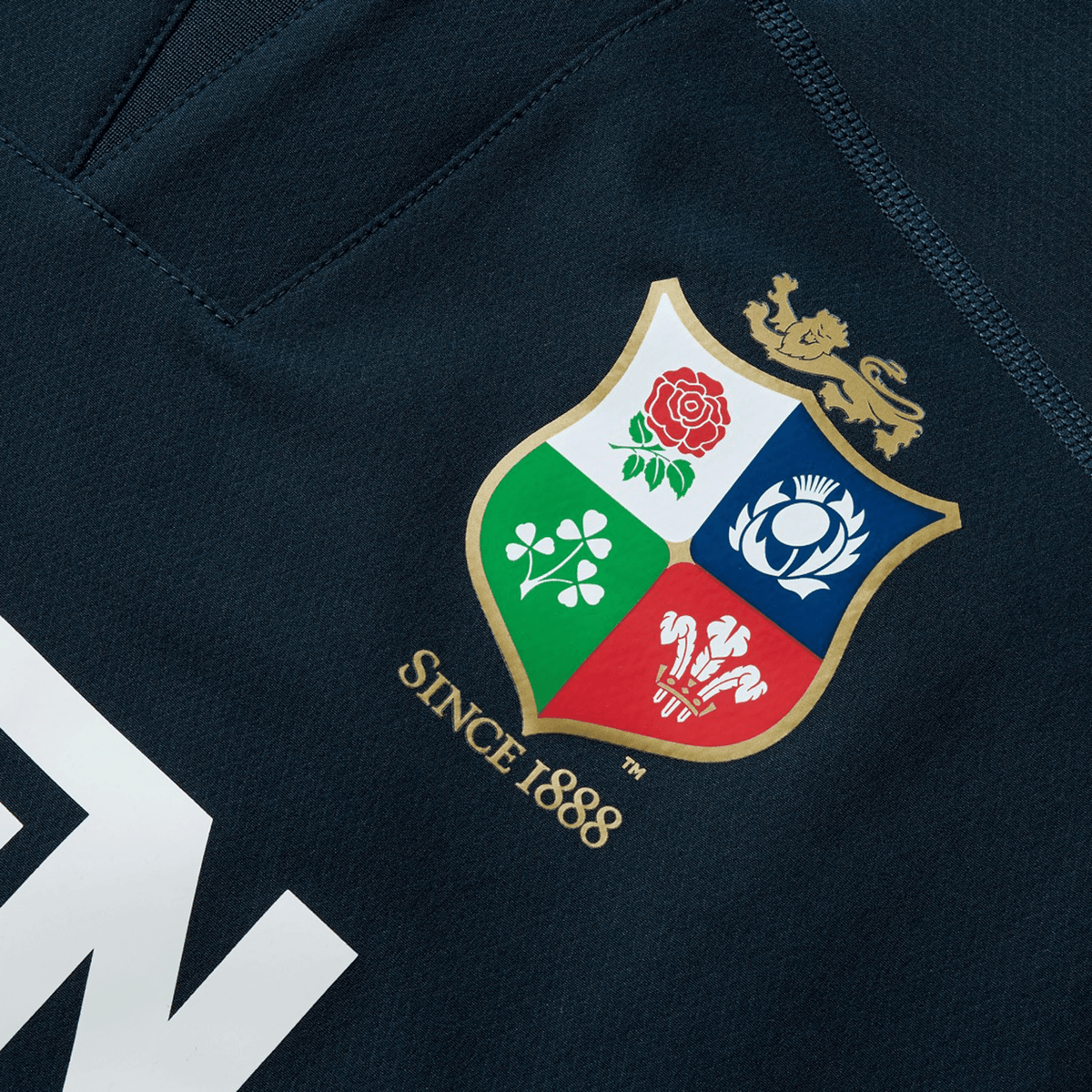A close-up of a navy blue, water-resistant fabric showcases a vibrant crest featuring a lion and four emblems, along with the text "SINCE 1888," reminiscent of the iconic British &amp; Irish Lions 25 Drill Top by Canterbury.