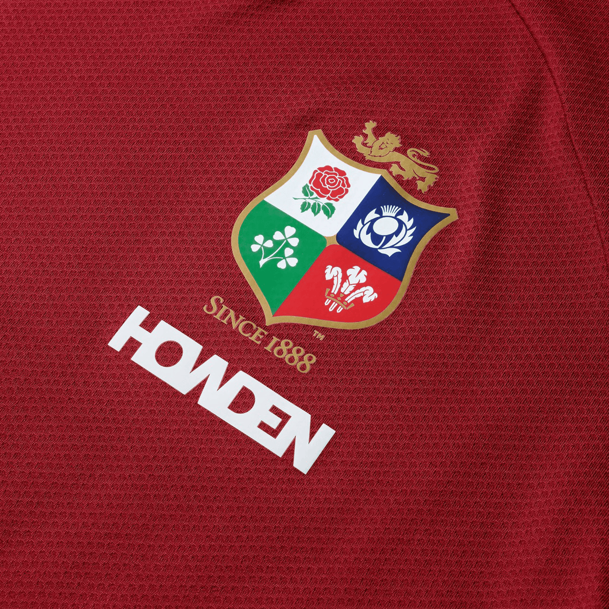 Close-up of a red sports jersey with vibrant imagery, displaying a shield adorned with four emblems and the text "Since 1888" above "Howden," capturing the iconic style of Canterbury's British &amp; Irish Lions 25 Everest Tee.