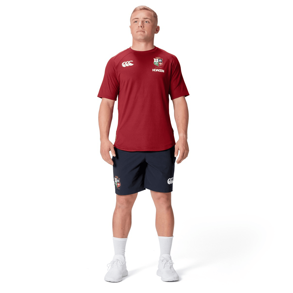 A person wearing a Canterbury British &amp; Irish Lions 25 Everest Tee, navy shorts, white socks, and sneakers stands against a plain white background.