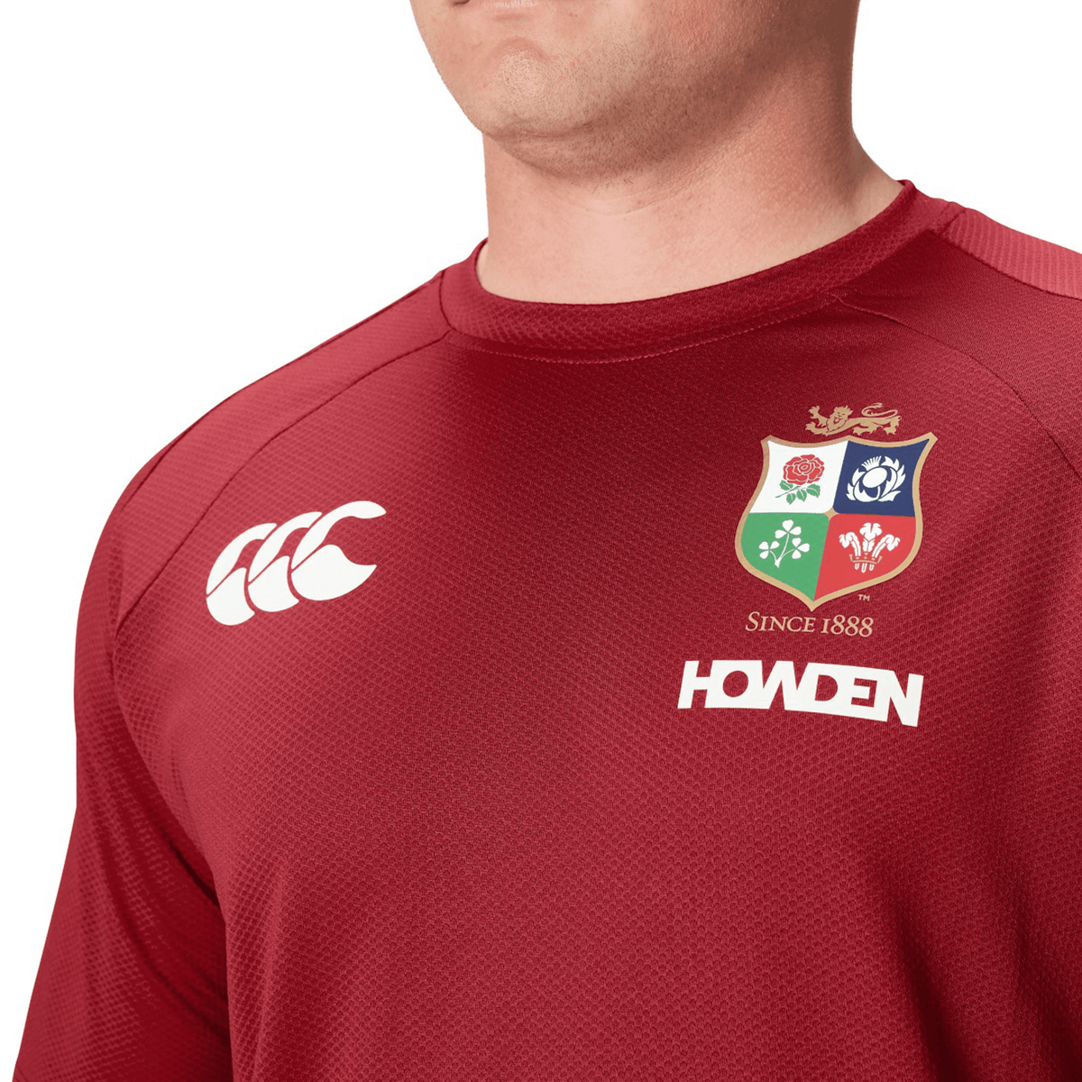 A close-up of someone wearing the red British &amp; Irish Lions 25 Everest Tee by Canterbury, highlighting its distinctive logos. The iconic emblem of the British &amp; Irish Lions is proudly displayed, with the Canterbury design and Howden sponsor name standing out.