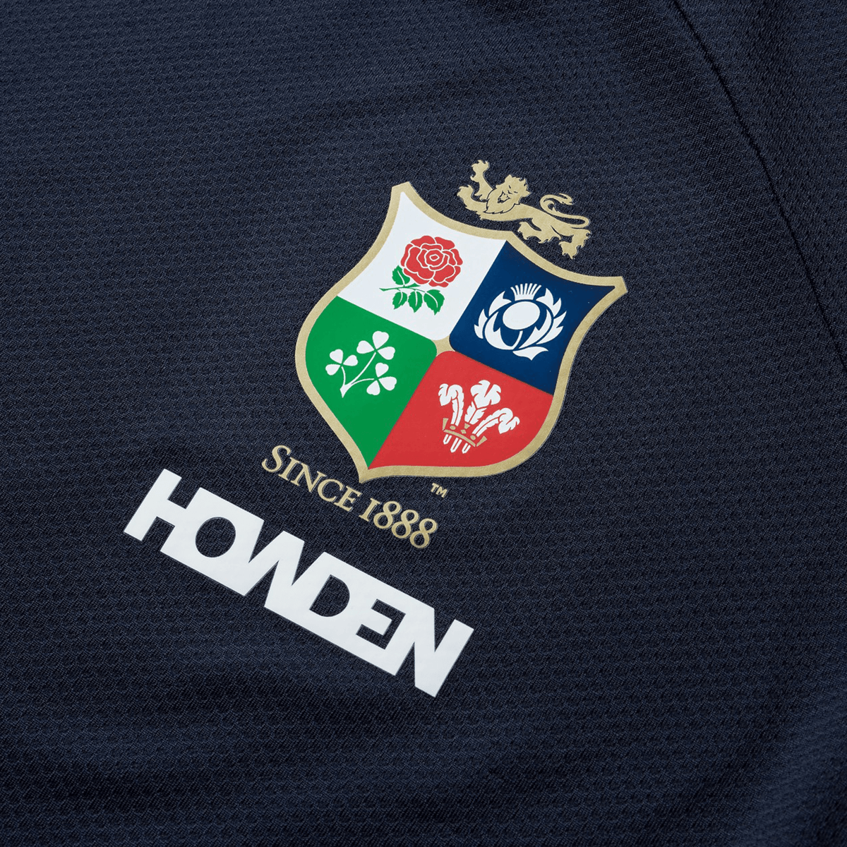 The British &amp; Irish Lions 25 Everest Tee by Canterbury, in navy, captures the essence of the British &amp; Irish Lions heritage. It showcases a crest adorned with a lion, rose, thistle, and clover alongside the inscription "Since 1888," with "Howden" positioned beneath the emblem.