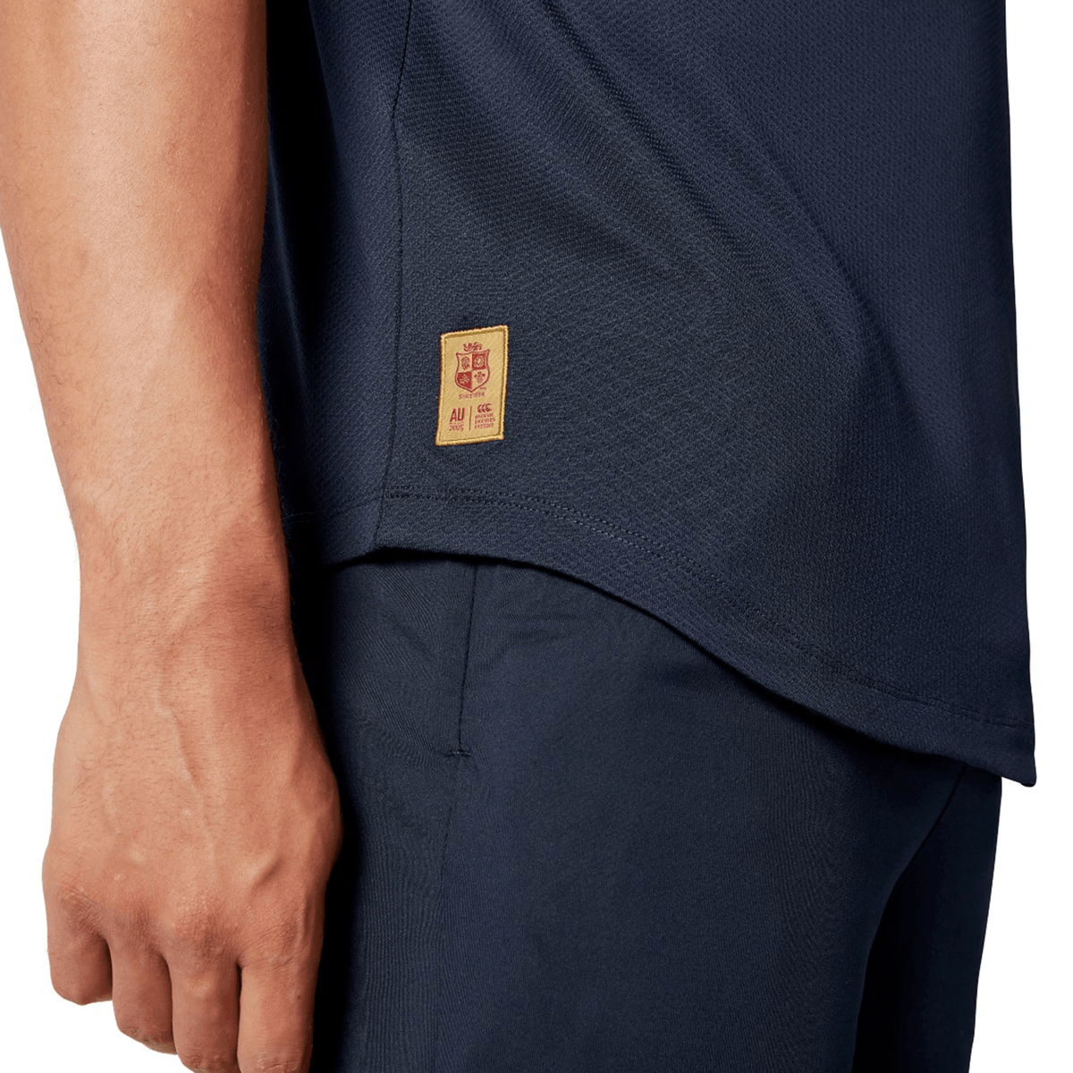 Close-up of a person wearing the British &amp; Irish Lions 25 Everest Tee by Canterbury and pants, featuring a small rectangular tag with a crest and numbers on the shirt's side, reminiscent of Canterbury's classic style.