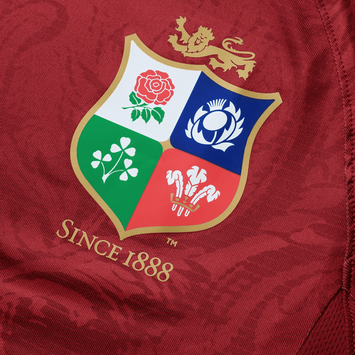 The British &amp; Irish Lions 25 Superlight Training Tee by Canterbury, crafted by Canterbury, features a red fabric with a gold-trimmed crest that displays symbols of a rose, thistle, shamrock, and three feathers beneath a lion. The text reads &quot;Since 1888.