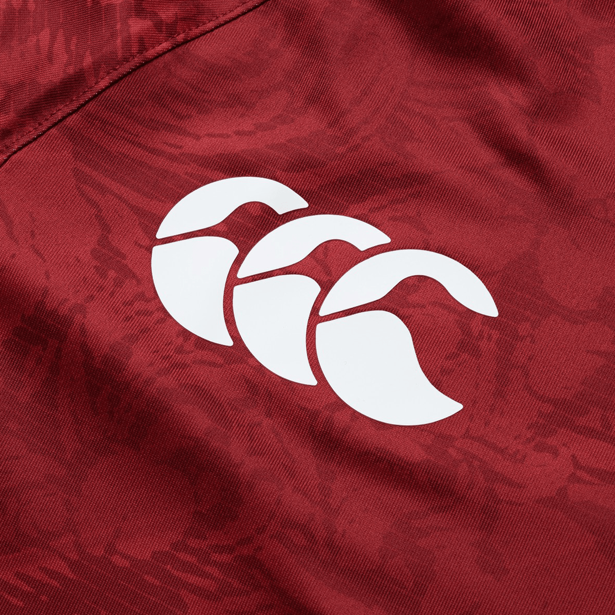 Close-up of a red fabric from the British &amp; Irish Lions 25 Superlight Training Tee by Canterbury, showcasing a white, three-leaf logo reminiscent of the iconic British &amp; Irish Lions design.