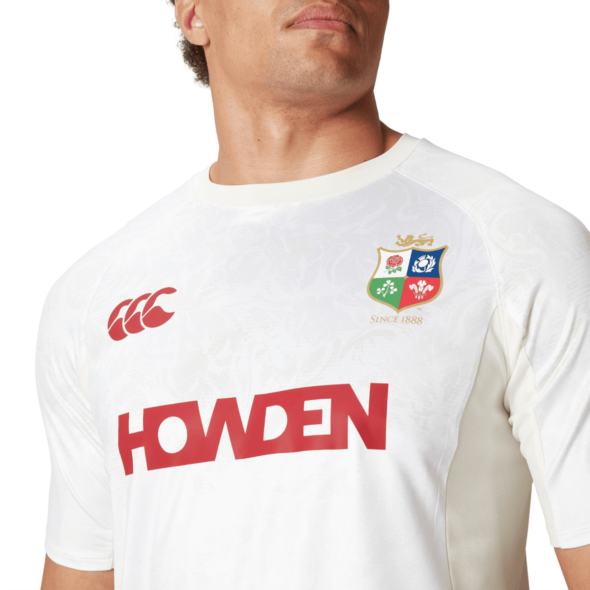 The individual wears a white British &amp; Irish Lions jersey, featuring a logo and &quot;HOWDEN&quot; on the front, comparable to Canterbury&#39;s craftsmanship in their 25 Superlight Training Tee.