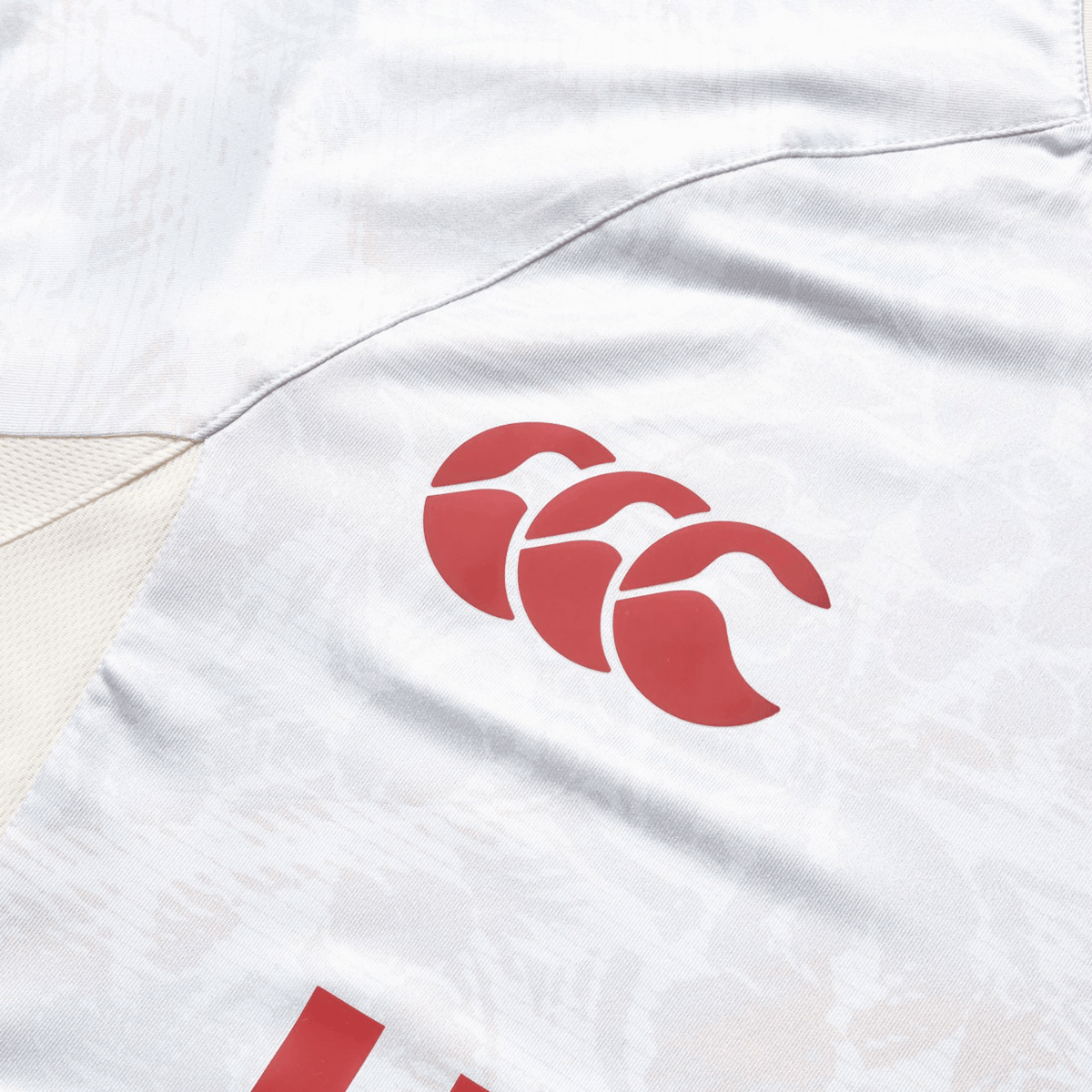 Close-up of a white fabric sports jersey with a red logo featuring three stylized letter C&#39;s in a wave pattern, reminiscent of the iconic British &amp; Irish Lions 25 Superlight Training Tee by Canterbury.