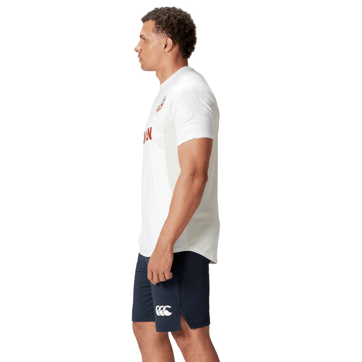 A person wearing a white British &amp; Irish Lions 25 Superlight Training Tee by Canterbury and navy shorts stands facing left against a plain background.