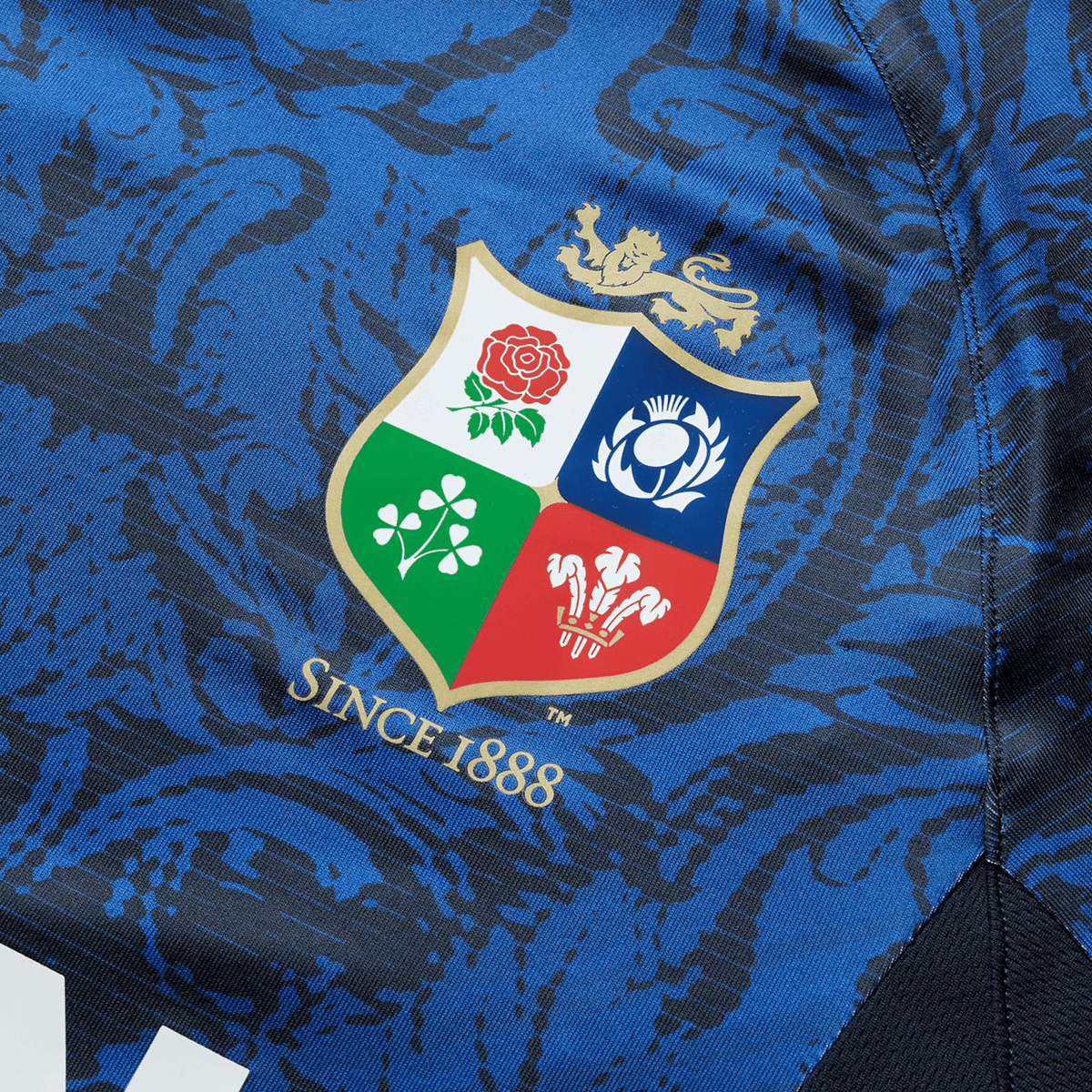 Close-up of the British &amp; Irish Lions 25 Superlight Training Tee by Canterbury in blue, highlighting its detailed texture. The tee features a multicolored shield logo adorned with floral and lion motifs, representing the British &amp; Irish Lions, along with the statement &quot;Since 1888&quot; located below.