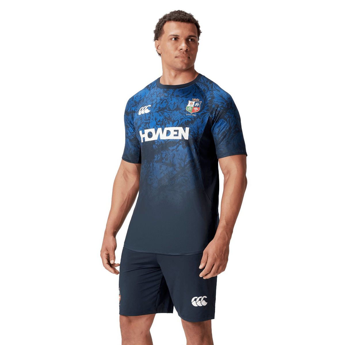 A man dons a British &amp; Irish Lions 25 Superlight Training Tee by Canterbury, featuring &quot;Howden&quot; and Canterbury logos, while he gazes thoughtfully to the side.