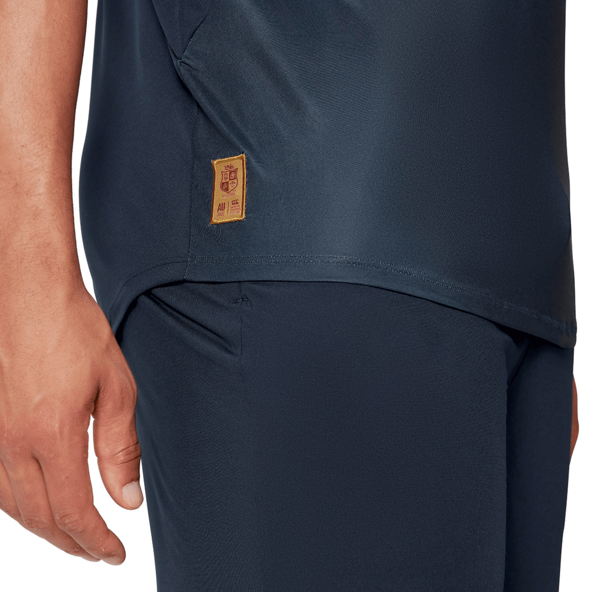 Close-up of a person wearing the British &amp; Irish Lions 25 Superlight Training Tee by Canterbury in navy blue, showcasing part of their torso and arm. A small embroidered label with Chinese characters adds a distinctive flair, reminiscent of Canterbury&#39;s collaborations with the British &amp; Irish Lions.