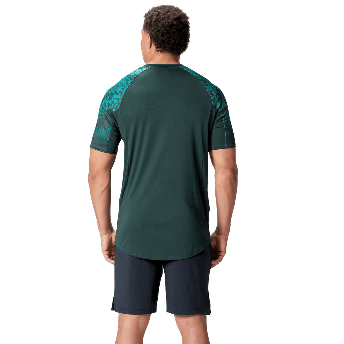 A man stands with his back to the camera, wearing a dark green British &amp; Irish Lions 25 Superlight Training Tee by Canterbury with patterned sleeves and black shorts.