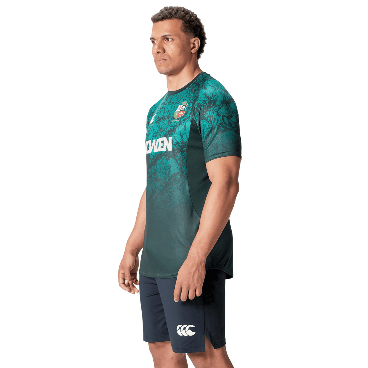 A man wearing a green British &amp; Irish Lions 25 Superlight Training Tee by Canterbury and navy shorts stands against a plain white background, embodying the spirit of Canterbury and the iconic British &amp; Irish Lions.