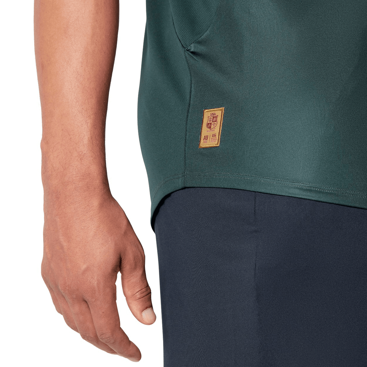 A person wearing a British &amp; Irish Lions 25 Superlight Training Tee by Canterbury in green, which features a small logo on the side, paired with dark pants.