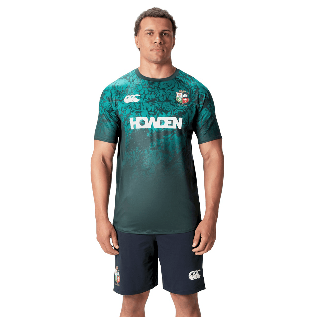 A man wearing a British &amp; Irish Lions Superlight Training Tee by Canterbury in green and black stands facing forward in his shorts.