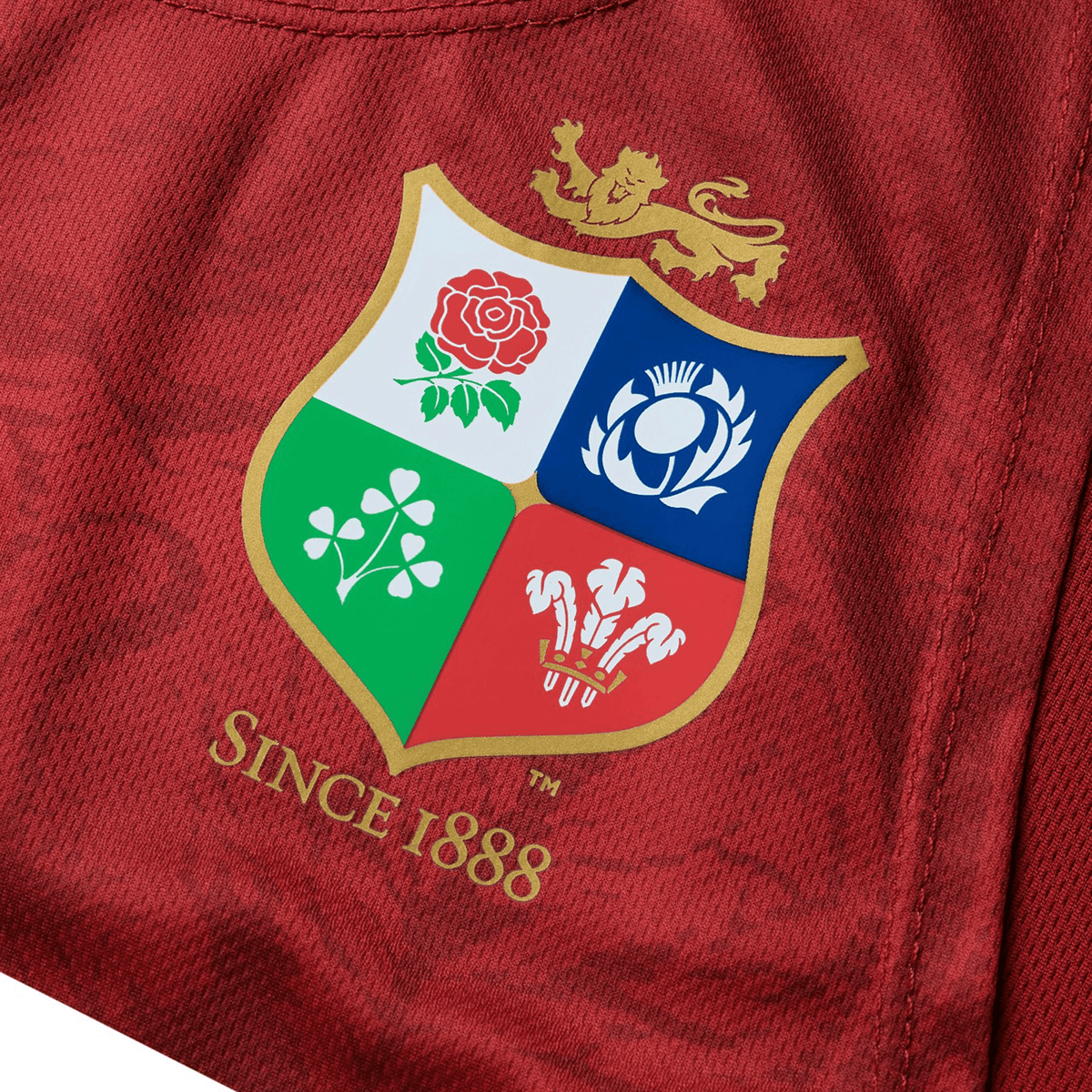 Close-up of a red fabric featuring the British &amp; Irish Lions emblem by Canterbury. It showcases four sections with symbols: a rose, a thistle, a shamrock, and a dragon, along with "Since 1888" text—a perfect detail for the iconic British &amp; Irish Lions 25 Poly Singlet design by Canterbury.