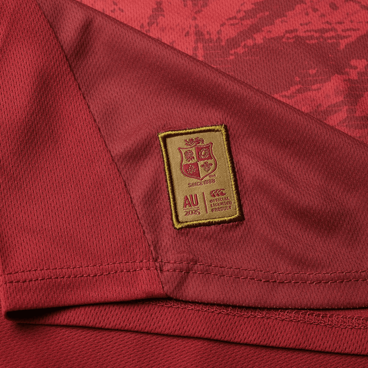 Close-up of a red Canterbury British &amp; Irish Lions 25 Poly Singlet, showcasing a gold patch with a shield design, the text "AU 2005," and various emblems that capture the iconic style linked to the British &amp; Irish Lions.