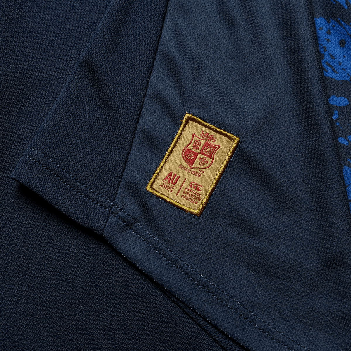 A close-up view of the British &amp; Irish Lions 25 Poly Singlet by Canterbury reveals a dark fabric design adorned with a small embroidered patch, showcasing a crest and text details in gold and red that capture the classic elegance associated with the British &amp; Irish Lions.