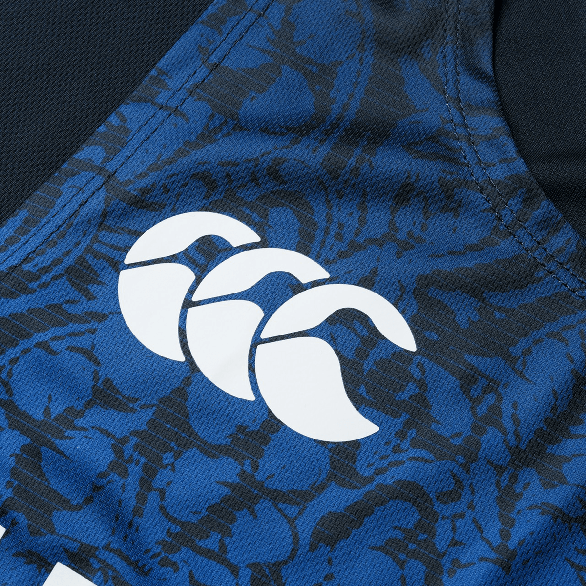 Close-up of a blue and black patterned fabric with a white logo featuring three overlapping curved shapes, reminiscent of the iconic designs on the British &amp; Irish Lions 25 Poly Singlet by Canterbury.