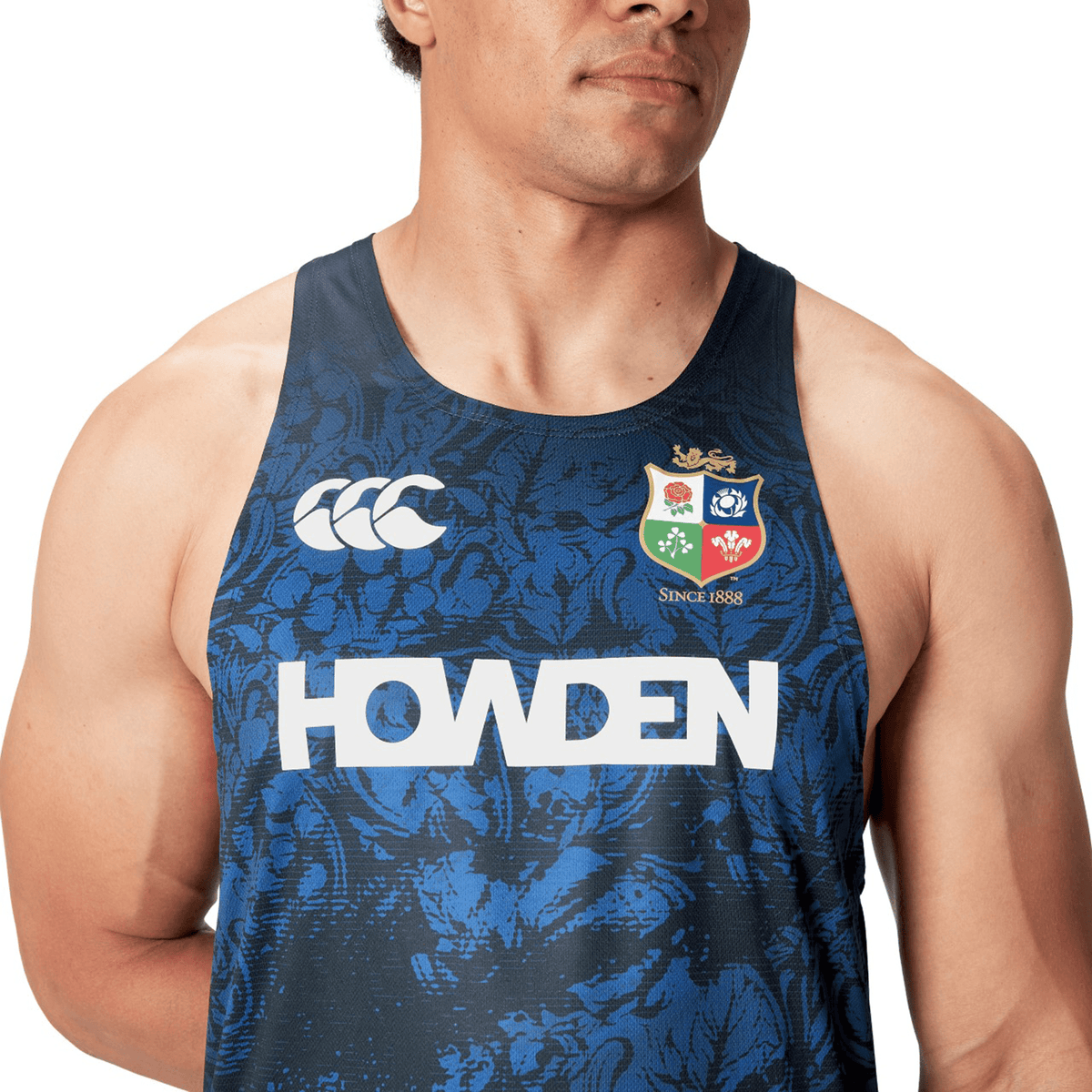 A man wearing the British &amp; Irish Lions 25 Poly Singlet by Canterbury, featuring a dark blue design with patterns, and showcasing both the Canterbury logo and British &amp; Irish Lions emblem, alongside the text "Howden.