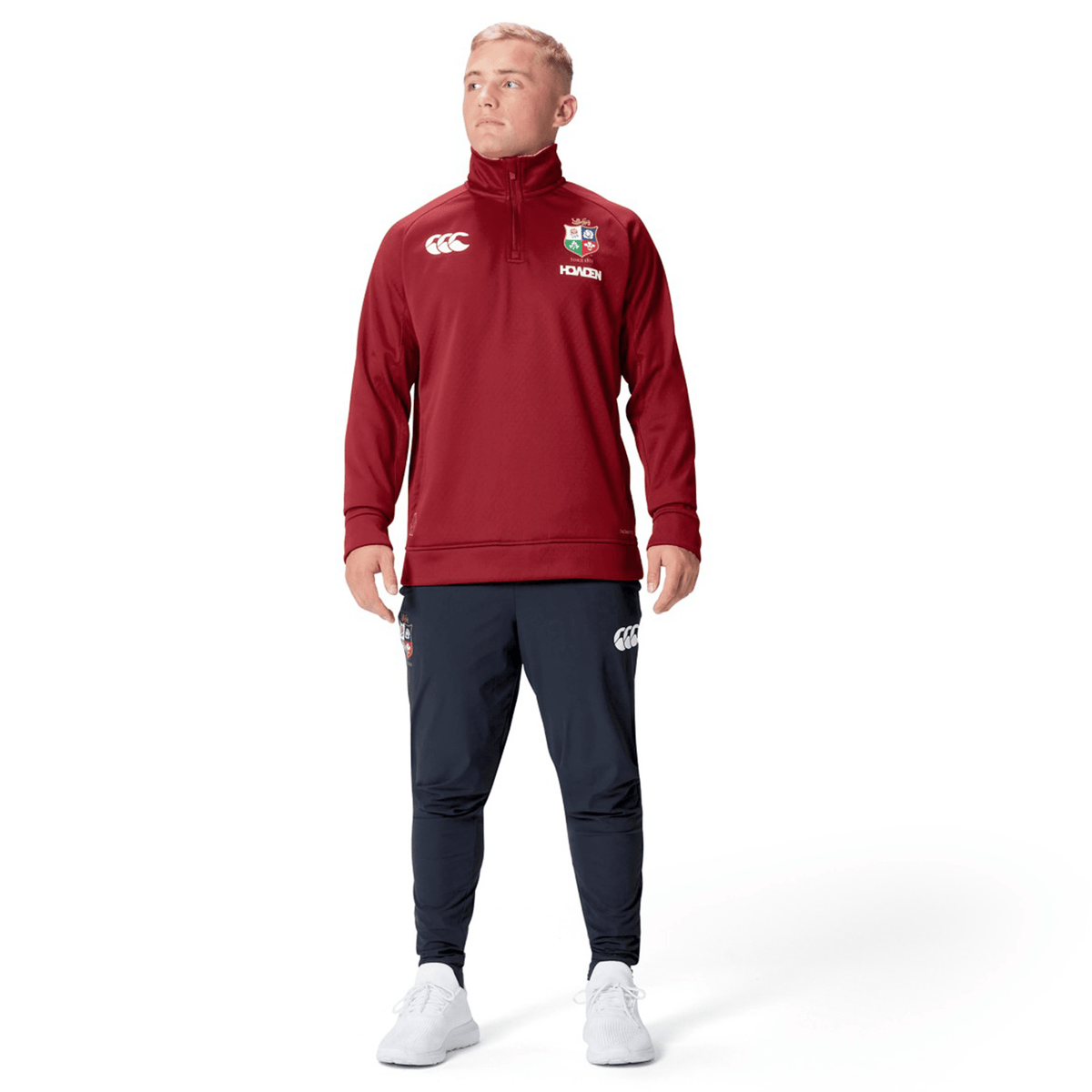 A person wearing the British &amp; Irish Lions 2025 1/4 Zip Fleece by Canterbury in red and navy pants, standing and gazing to the side against a plain white background.