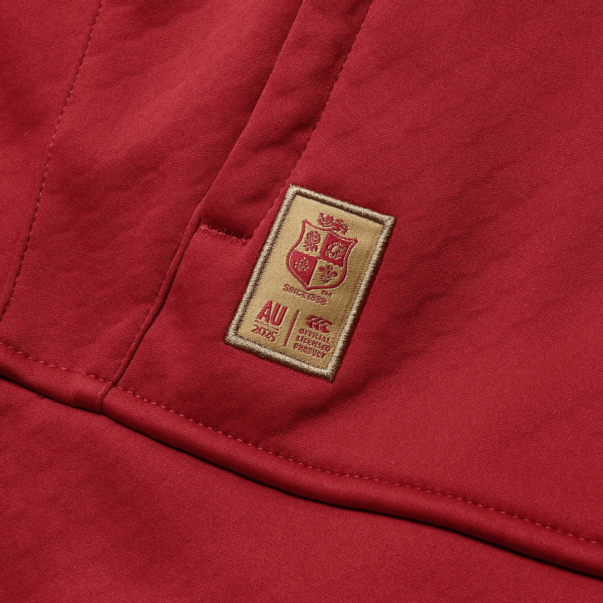 A red fabric with an embroidered patch showcasing a coat of arms, the text &quot;AU 2023,&quot; and the phrase &quot;Ref. Special Product.&quot; Inspired by the heritage and pride of the British &amp; Irish Lions, this exclusive design is ideal for pairing with Canterbury&#39;s British &amp; Irish Lions 2025 1/4 Zip Fleece.