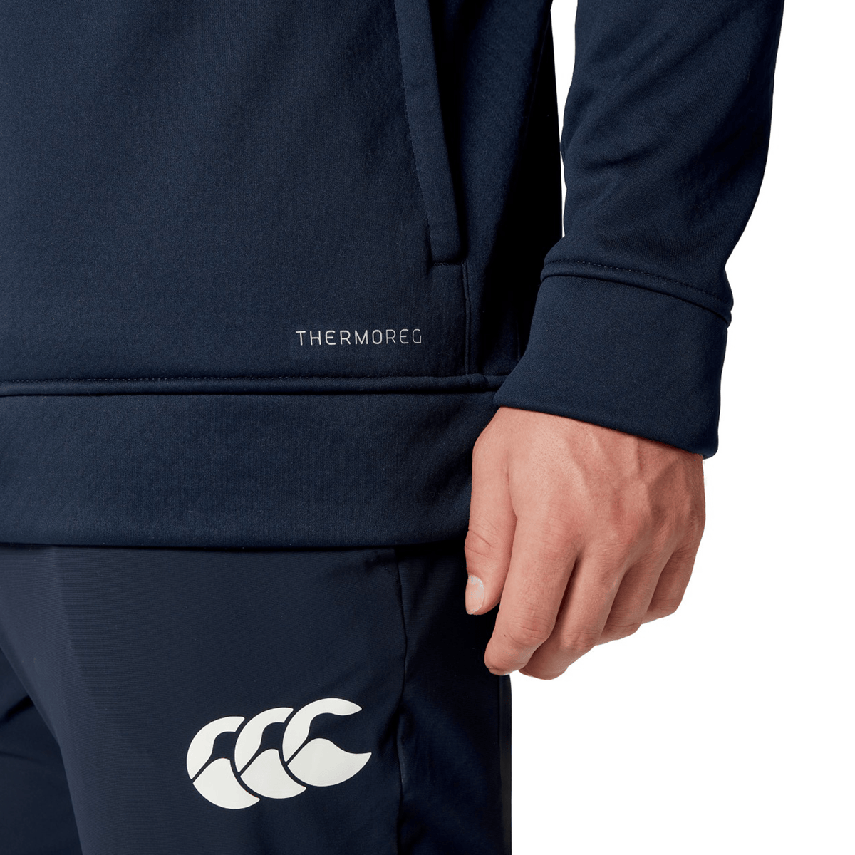 Close-up of a person wearing a navy sports outfit, showcasing the "THERMOREG" label on the top and a white logo on the pants. The British &amp; Irish Lions 2025 1/4 Zip Fleece by Canterbury perfectly complements their look, evoking an athletic spirit reminiscent of Canterbury's celebrated apparel for the British &amp; Irish Lions.