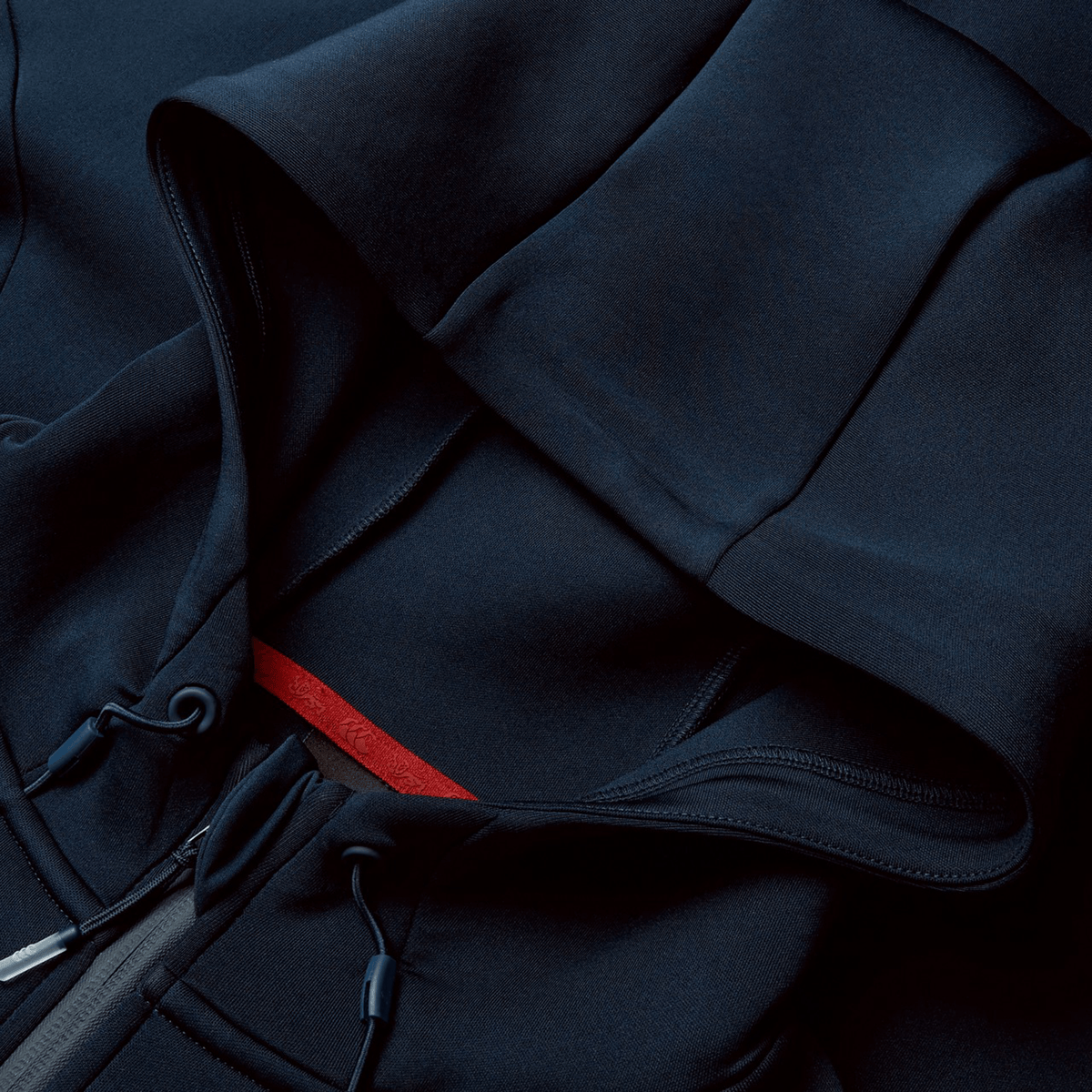 Close-up of the navy blue British &amp; Irish Lions 2025 Everest Hoodie by Canterbury, showcasing its hood and adjustable drawstrings, laid flat. Made from recycled polyester, it includes a small red tag near the neckline.