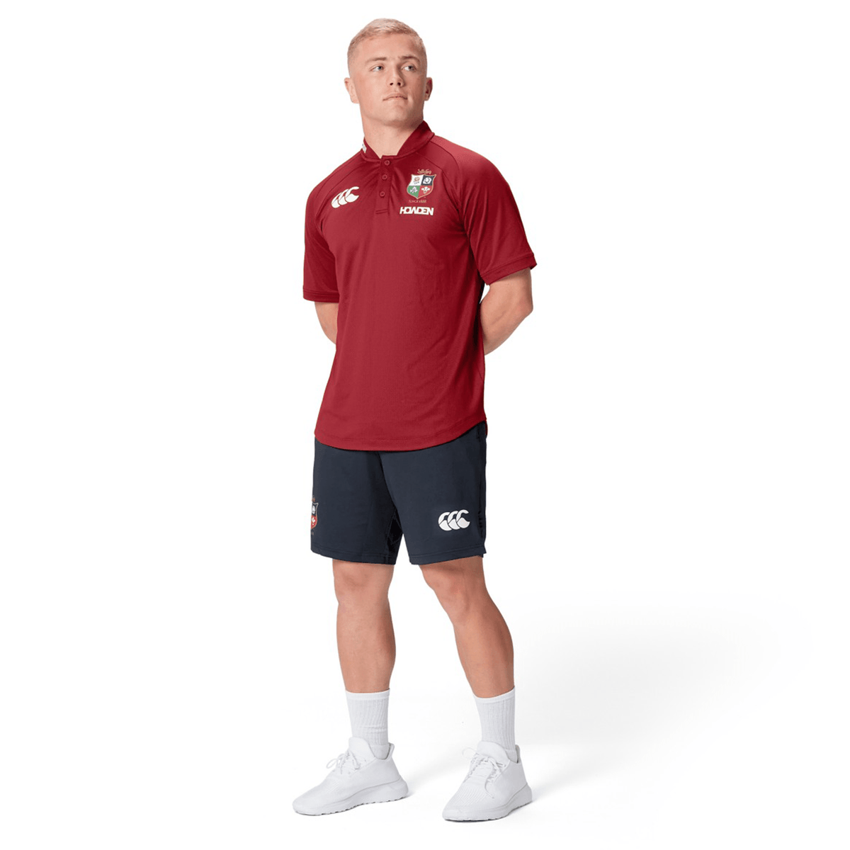 A person wearing the British &amp; Irish Lions 25 Poly Polo by Canterbury, coupled with black shorts, stands with hands behind their back and gazes to the side on a white backdrop, capturing the timeless style of Canterbury and the vibrant heritage of the British &amp; Irish Lions.