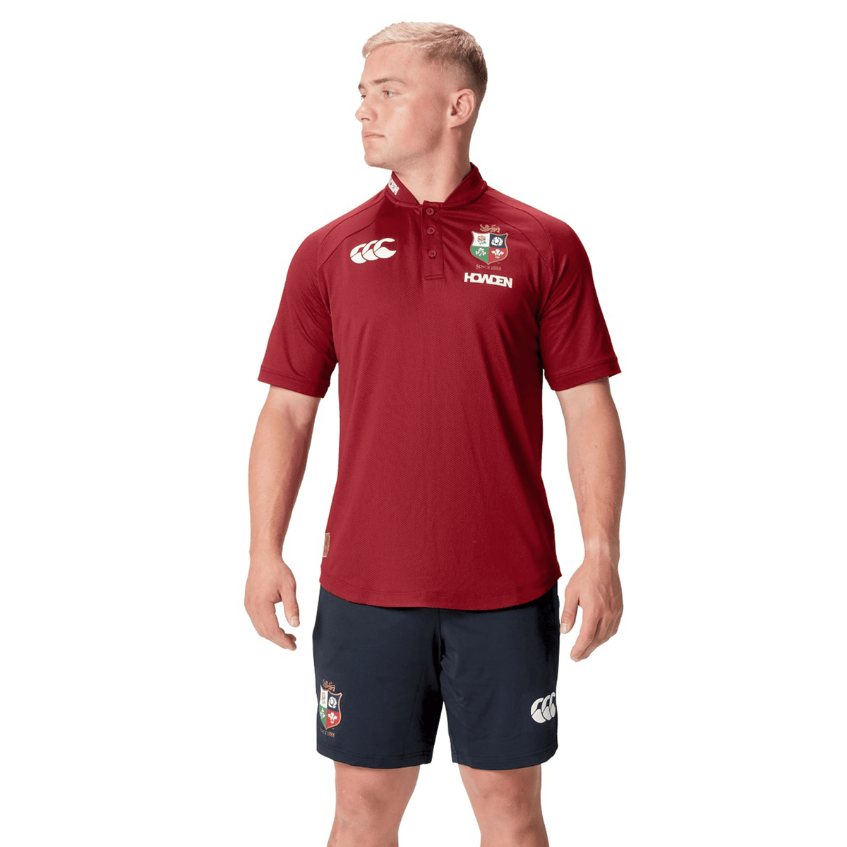 Dressed in the British &amp; Irish Lions 25 Poly Polo by Canterbury in maroon and navy logo shorts, a person stands against a white background, perfectly capturing the classic style of the collection.