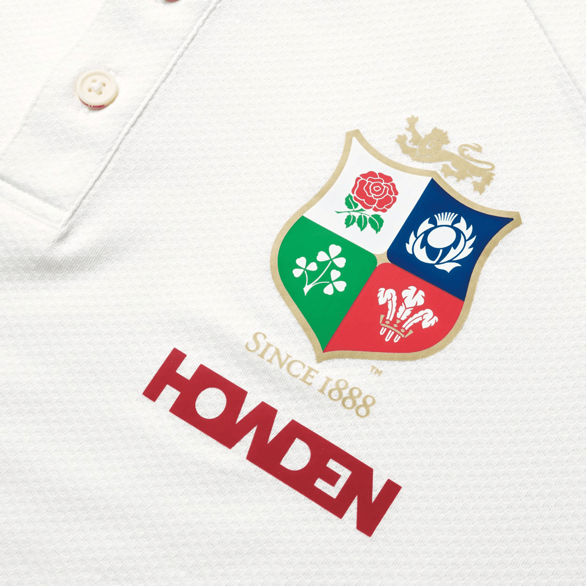 Close-up of the British &amp; Irish Lions 25 Poly Polo by Canterbury, showcasing a four-part shield crest with a rose, thistle, shamrock, and dragon. Decorated with "SINCE 1888" and "HOWDEN" in red lettering, this quick-drying polo also features an embossed BIL neck tape for an extra touch of style.