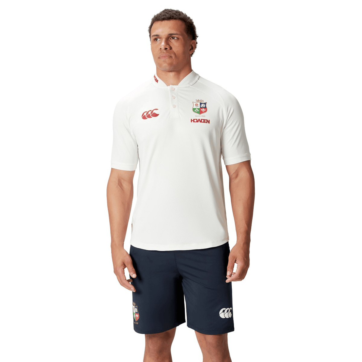Dressed in a British &amp; Irish Lions 25 Poly Polo by Canterbury and navy shorts, an individual stands against a plain background, capturing the classic style of dedicated Lions fans.
