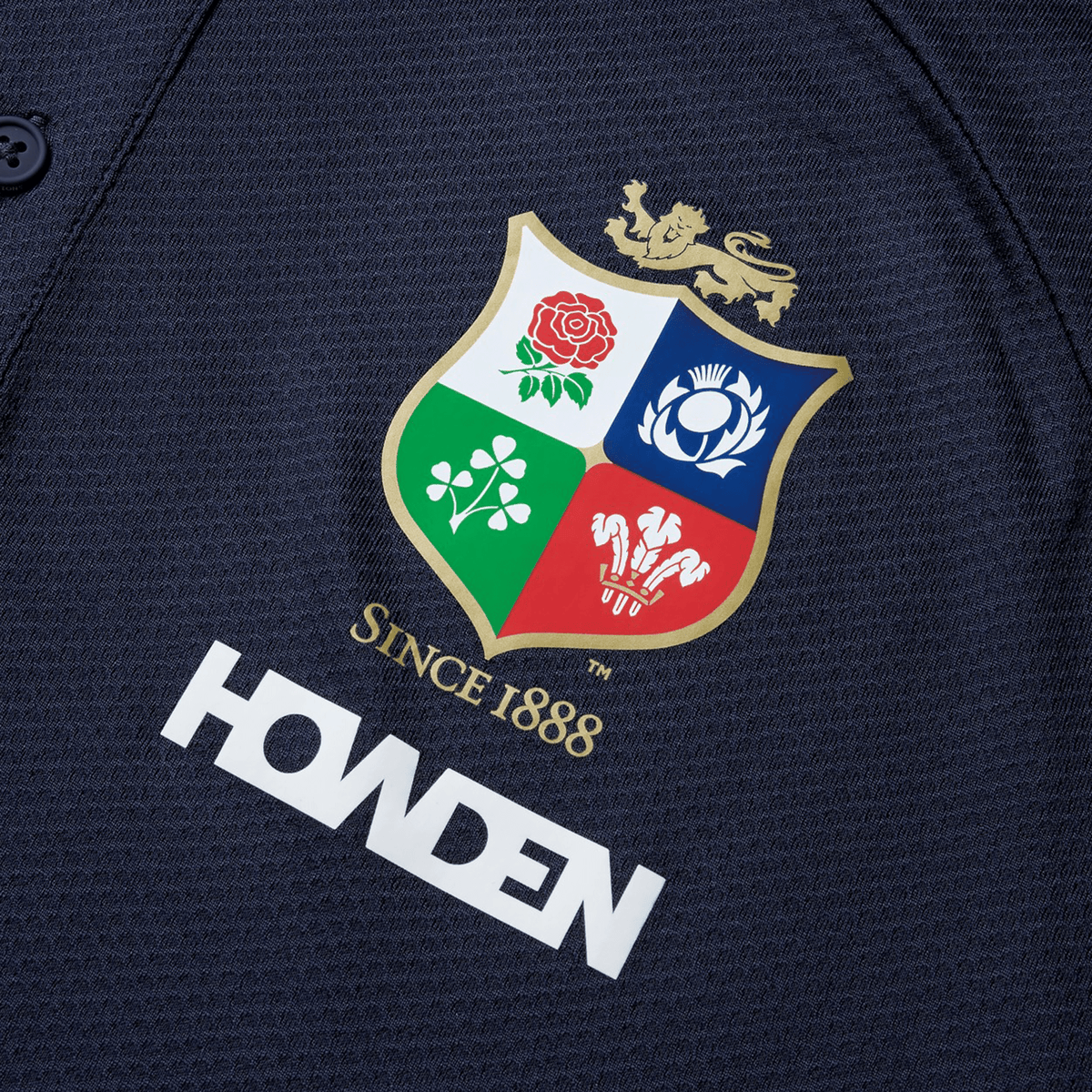 Close-up of a British &amp; Irish Lions 25 Poly Polo by Canterbury, made from quick-drying fabric, showcasing the team's crest and "Howden" sponsor logo on a dark background.