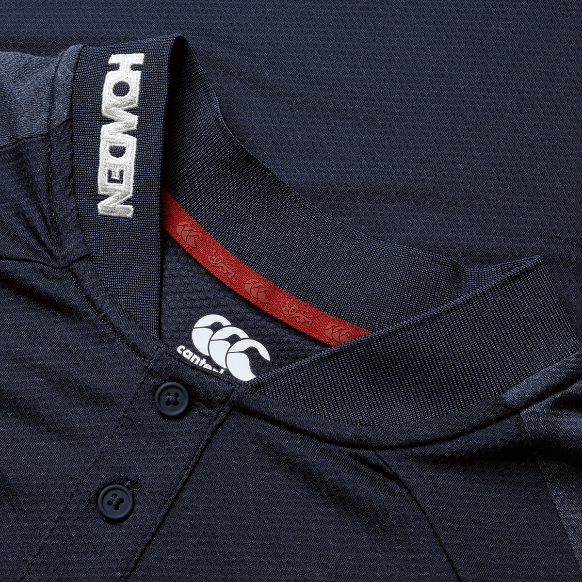 Close-up of the British &amp; Irish Lions 25 Poly Polo by Canterbury, showcasing "HONDEN" on the collar and Canterbury logo, crafted from quick-drying, breathable fabric. The design is inspired by a dark rugby jersey and features red inner neck detailing.