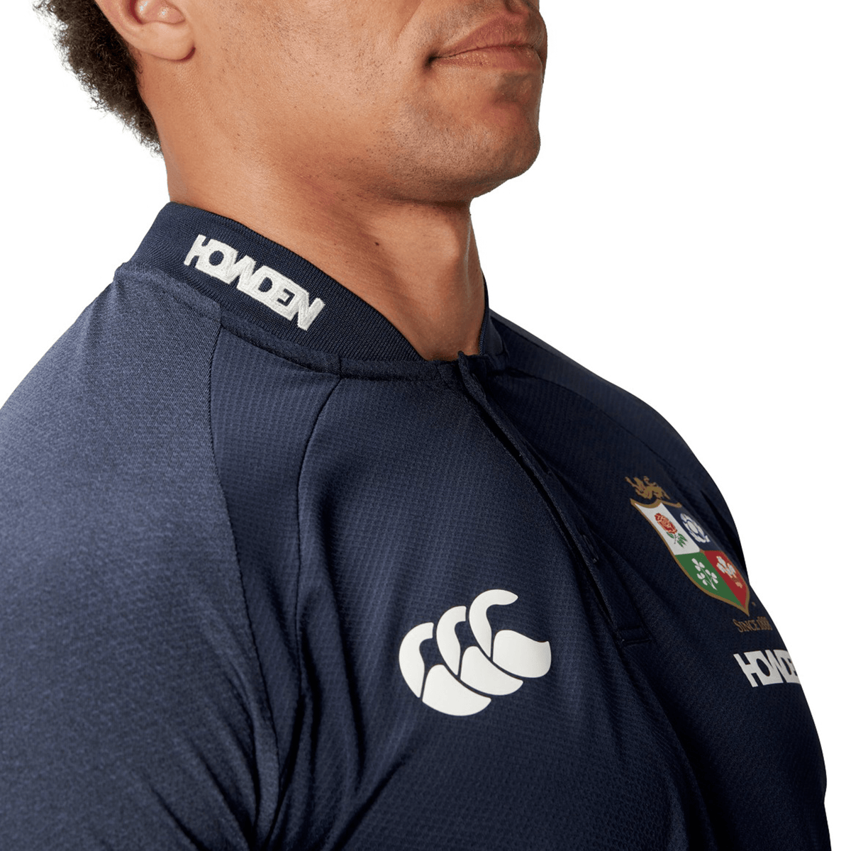 A person wearing the British &amp; Irish Lions 25 Poly Polo by Canterbury, a navy sports jersey featuring white logos on the chest and collar, crafted from quick-drying, breathable fabric.