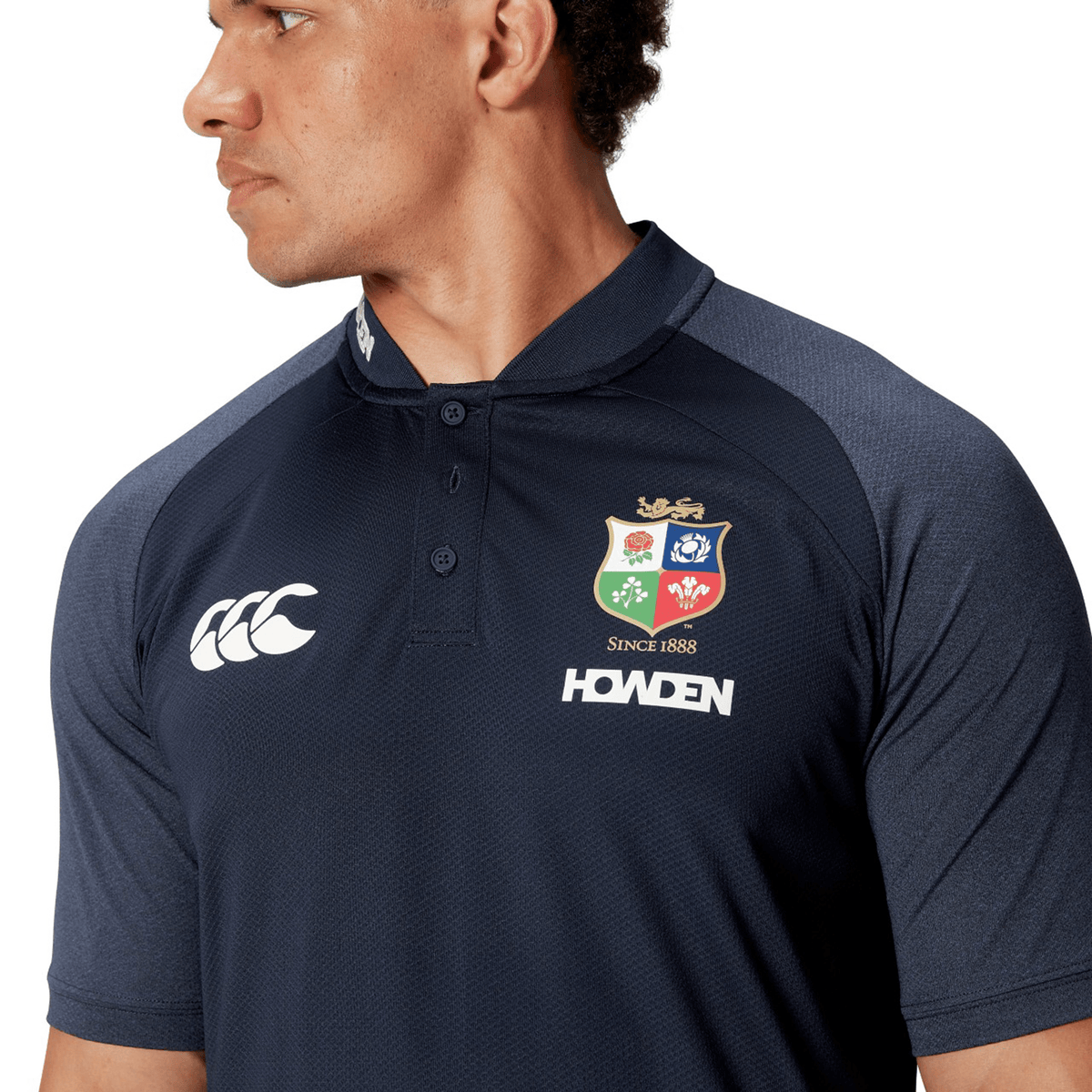 A person wearing a dark blue Canterbury British &amp; Irish Lions 25 Poly Polo, featuring logos and made from quick-drying fabric, glances to the side.