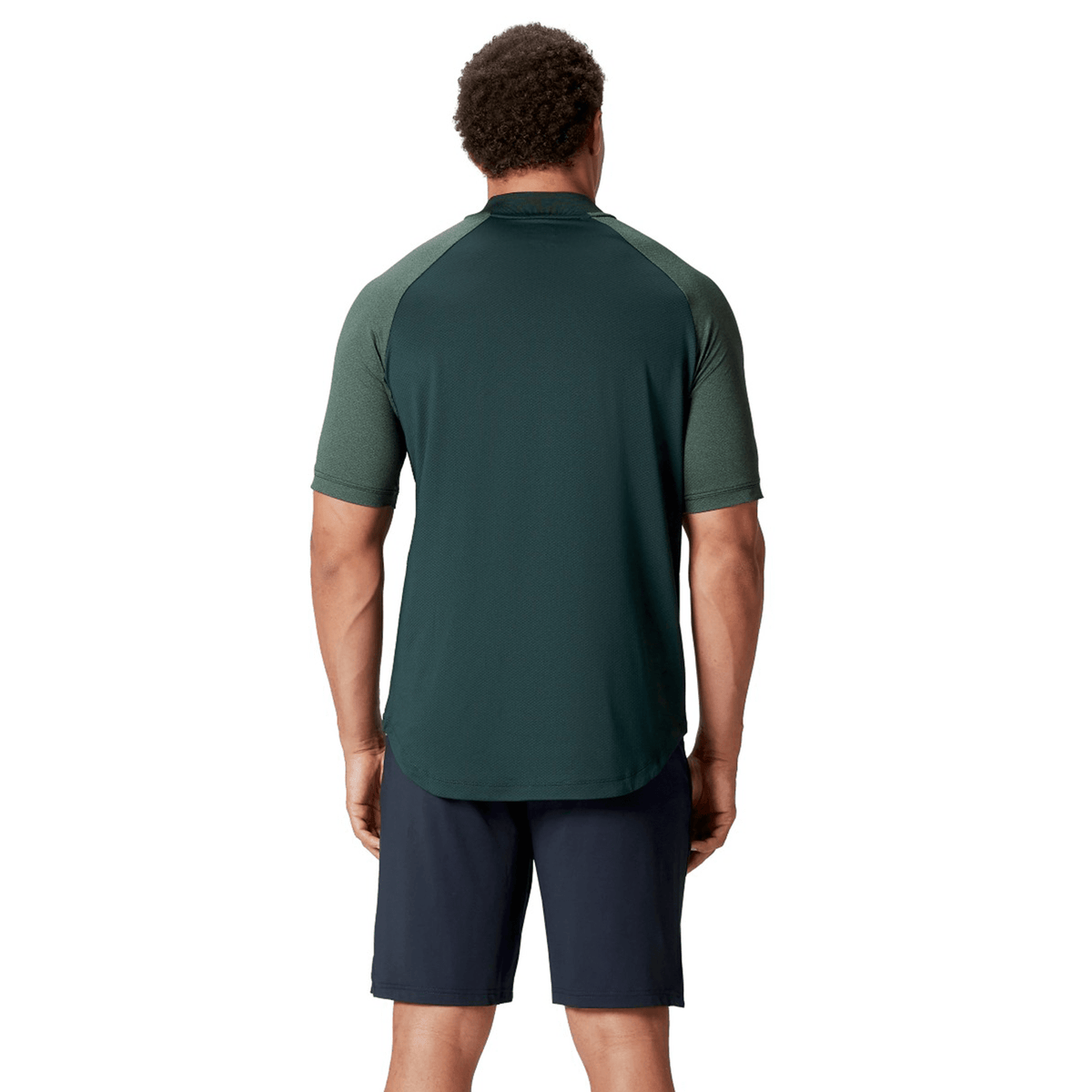 A person stands with their back turned, wearing a dark green British &amp; Irish Lions 25 Poly Polo from Canterbury, crafted from quick-drying fabric, paired with dark shorts, set against a plain white background.