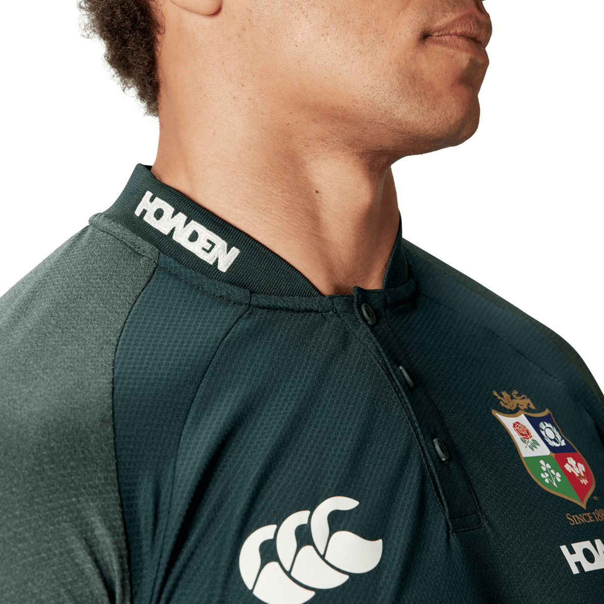 A person wearing a British &amp; Irish Lions 25 Poly Polo crafted by Canterbury, featuring a dark green color, iconic emblems, and "HONDEN" on the collar, made with quick-drying fabric perfect for any match day.