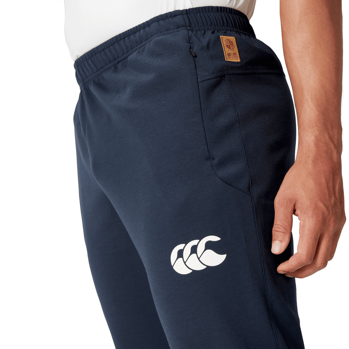Close-up of a person wearing British &amp; Irish Lions 25 Training Pants by Canterbury in navy blue, showcasing a white logo and the British &amp; Irish Lions emblem on the waistband.