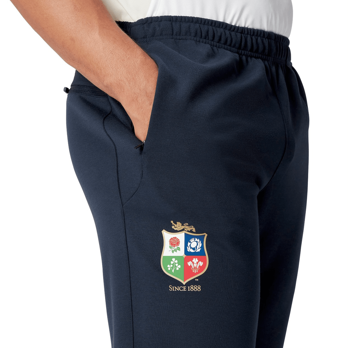 A close-up of someone wearing the British &amp; Irish Lions 25 Training Pants by Canterbury, showcasing a vibrant embroidered crest with four emblems and "SINCE 1888" text on the side, is seen.